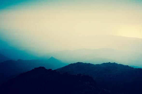 Photo of mountain silhouettes in atmospheric mist and half-light, with a dominant bluish tint