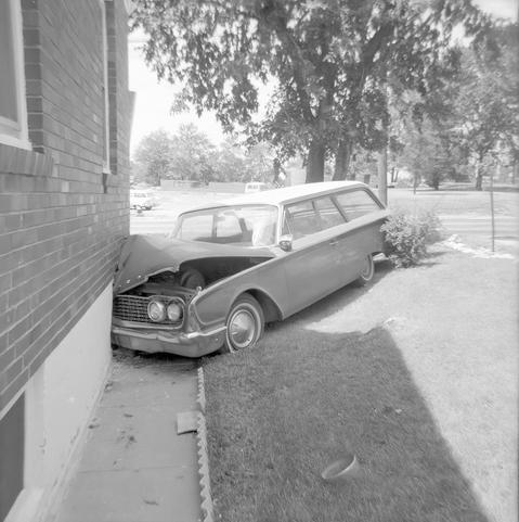 A station wagon that has crashed into the corner of a brick building.