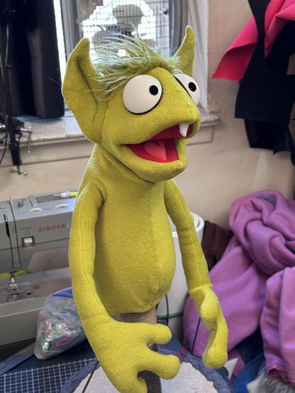 Full body view of a green goblin hand puppet with large eyes and a single tooth