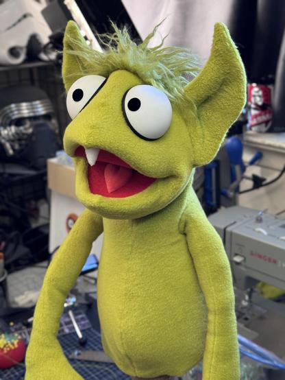 Left closeup view of a green goblin hand puppet with large eyes and a single tooth