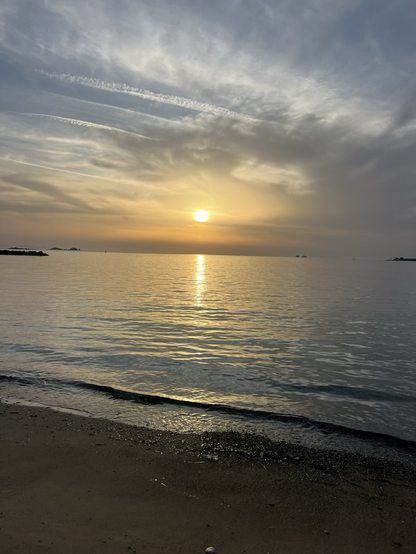A peach coloured sunset over a calm, slate blue Aegean Sea in  Paroikia, Paros. Sandy beach in foreground .