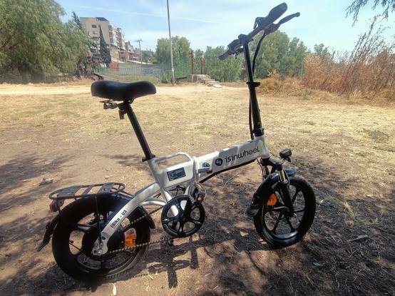 an ebike parked over the dirty road in the front, and in the background, trees, buildings an a holding bridge.