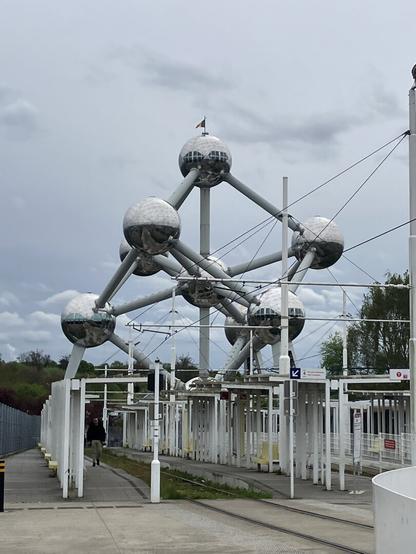 The Atomium monument in Brussels in the background, the metro tacks in the first place, below. Grey cloudy sky. The Atomium is like a big cubic structure with spheres in its angles and in the middle, it reproduces in big scale an atom of iron.