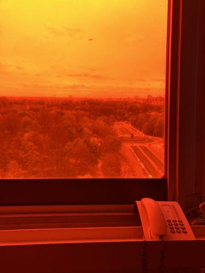 Window inside the Atomium. You can see the landscape through it from above. The window glass is covered with a red filter, making everything reddish. There is an old phone below the window.