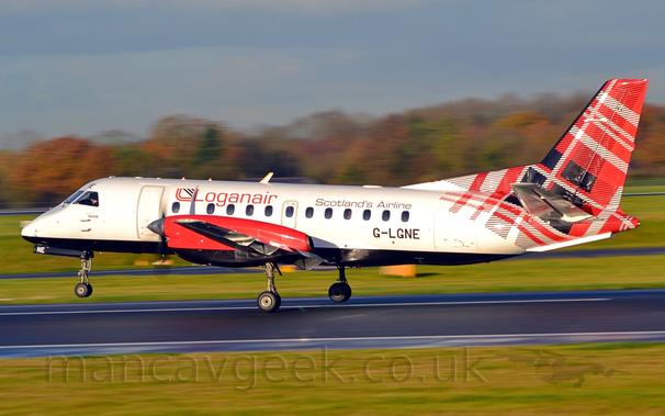 Side view of a white, twin propellor-engined airliner  just leaving a black runway, moving from right to left, it's nosewheel in the air, it's right main gear just centimetres off the runway, it's left wheel still on the ground.
The plane has a black belly, and red engine pods mounted over the wings, the propellors in front of the engines little more than black smears.
There are red "LoganAir" titles on the upper forward fuselage, with smaller "Scotlands Airline" titles in black on the upper rear.
The registration "G-LGNE" is on the lower rear fuselage, also in black.
The rear fuselage and tail is covered in a red, black, and white tartan pattern.
A wide strip of green grass fills the foreground, with more grass on the other side of the runway leading up to blurred trees in the distance, under grey-blue sky.