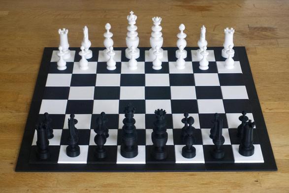 A 3D printed chess set and chess board on a tabletop. The set is bright white and coal black.