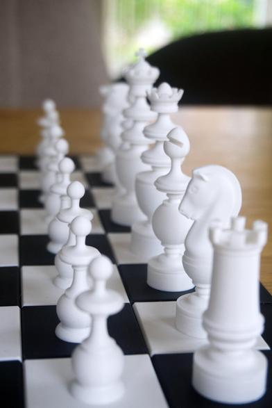 Closeup of a 3D printed chess set and chess board on a tabletop. The photo focuses on the white pieces, photographed from a side view angle.