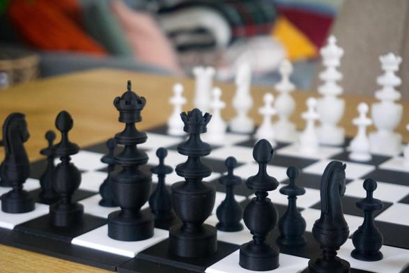 A 3D printed chess set and chess board on a tabletop. The set is bright white and coal black.