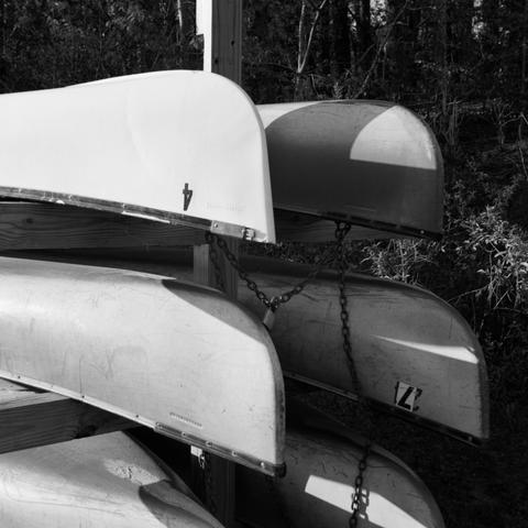 6 canoes on a rack, chained and locked together.  3 are in sun, 3 in shadow.
