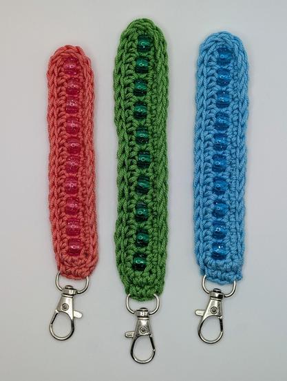 Three crochet fidget keychains laid out on a white background. From left to right; they are coral pink, apple green, and cerulean blue with matching beads.
