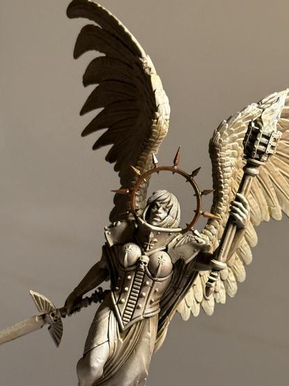 A detail of a 28mm-scale statue of a winged figure holding a torch and sword, with a spike brass halo