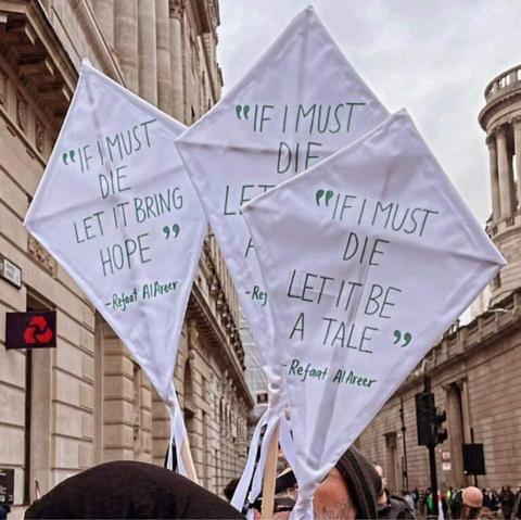 A photograph of people carrying white kites with the words, "If I must die, let it bring hope" - Refaat Alareer. The people are in a city, surrounded by official-looking buildings made of stone.