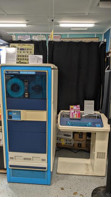 A very large vertical cabinet of a Data General Eclipse system on the left, with its magnetic tape unit towards the top. On its right, a terminal printer also from Data General.