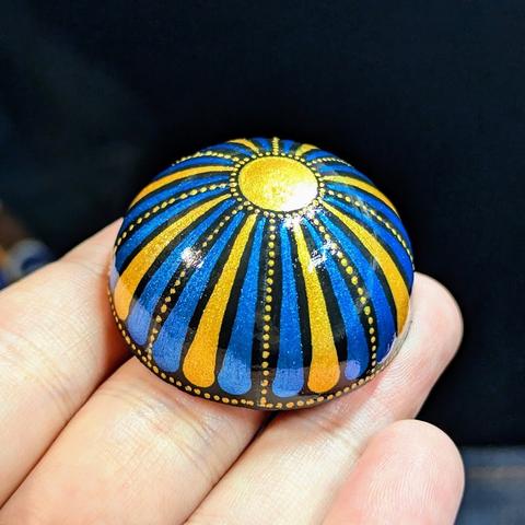 The same blue and gold magnet, but viewed from the side, showing the ends of the swooshes and a border made of tiny gold dots.