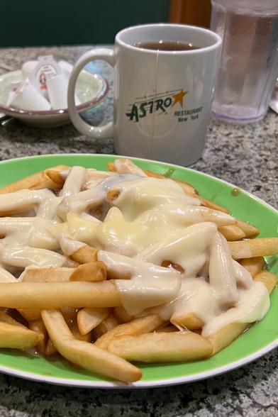A plate of disco fries- French fries covered in cheese and gravy. Sadly, this plate has a pale, almost white cheese, pale fries, and little gravy. All sitting on a green plate on a diner table top.