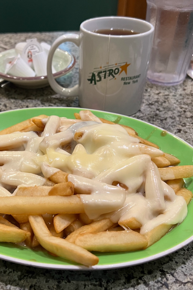 A plate of disco fries- French fries covered in cheese and gravy. Sadly, this plate has a pale, almost white cheese, pale fries, and little gravy. All sitting on a green plate on a diner table top.