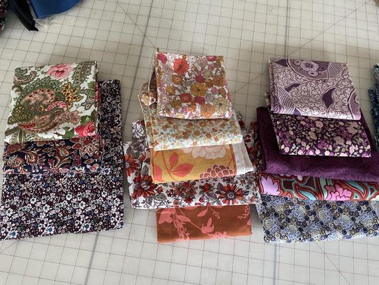 A spread of about a dozen different floral print cottons in warm tones of purple, orange, and red.