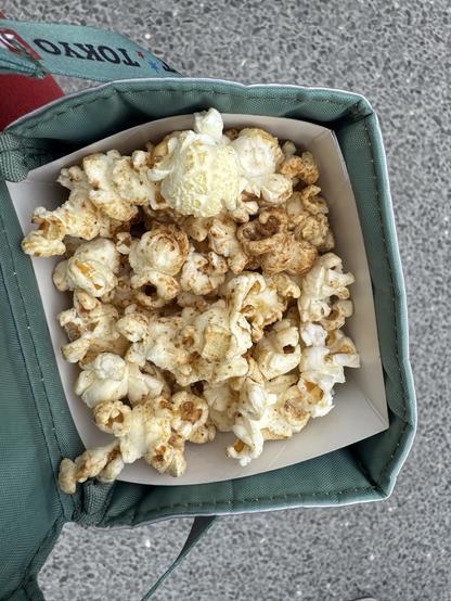Looking down at a box of popcorn. the popcorn has dark colored powder on top.