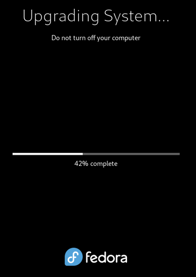 The Fedora screen during a system upgrade from 41 to 42, showing the progress is at 42%.

At the top it says "Upgrading System. Do not turn off your computer".

In the middle is a horizontal progress bar, beneath which is "42% complete".

At the bottom is the Fedora Linux logo, followed by "fedora". 

The screen is black, the font & graphics are white, except the logo is white font on a blue background.
