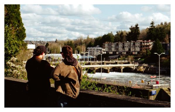 Two people talking with the Ballard Locks in the background.