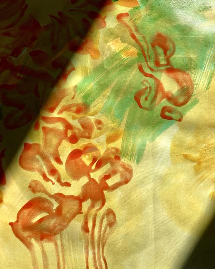 A section of a painting sketch on paper that is highlighted by a beam of sunshine. The sketch is a jumble of thinly painted, broad brushstrokes of pale yellow and pthalo green on a white background. Over the wash of yellow and green are several squiggly bursts of orange brushstrokes with drippy tails going down, like loose flames.
