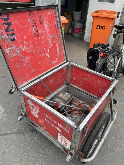 A bicycle with a box-shaped trailer photographed from behind. The side walls of the trailer are folded up. A lid is now fitted which can be locked when closed