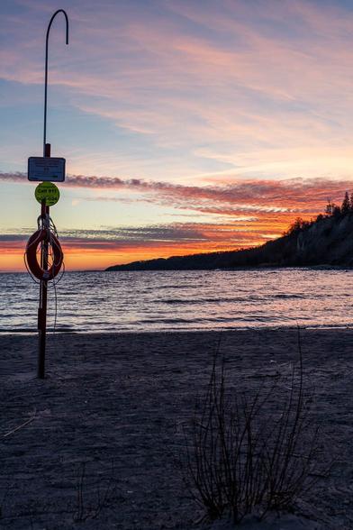 Sunset over Lake Ontario seen from Scarborough Bluffs Park, with a silhouetted lifebuoy post and warm colors in the sky.