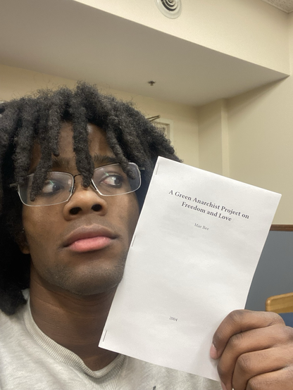 Me (spookyboi) holding a zine of A Green Anarchist Project on Freedom and Love by Mae Bee