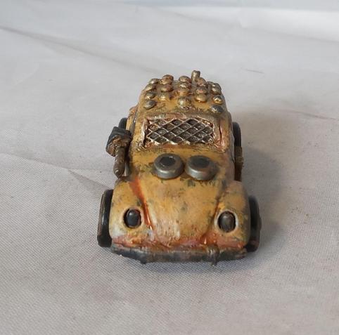 A Hot Wheels VW Beetle modified for the Gaslands game. Its mainly a rusty yellow, with a studded roof and a side-mounted machinegun. Front view.