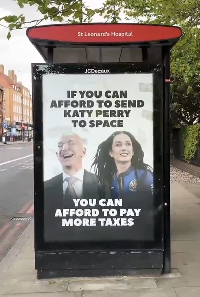 Ad on bus shelter, London. A smiling Jeff Bezos and Katy Perry in a spacesuit. Text reads 'If you can afford to send Katy Perry into space, you can afford to pay more taxes.'