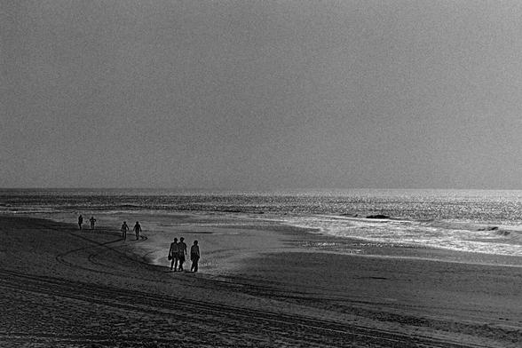 View of a beach with three groups of people walking along the shore