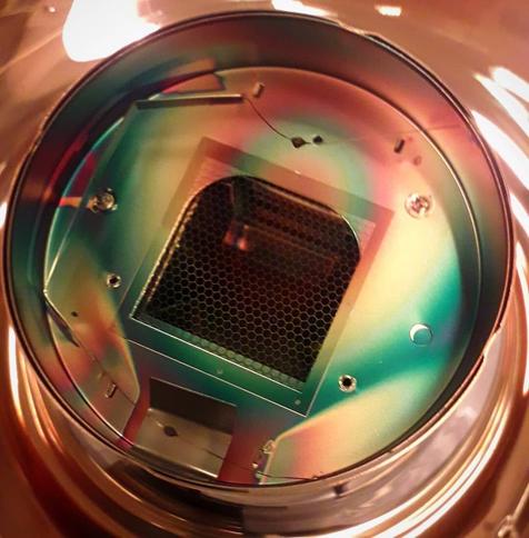 A train-tunnel shaped grid sits in front of the dynode chain of a photomultiplier tube, photographed from the top of the PMT, making everything have vivid green and orange hues.