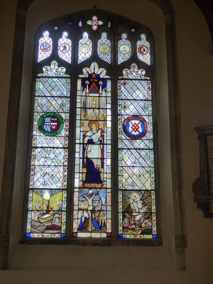 A backlit photo of a stained glass window. This circa 1840 window is believed to have been designed by Joseph Grant of Costessey. The centre light contains a painted panel of the Virgin Mary and Child whilst  the base lights display scenes of: The Nativity, Crucifixion and Ascension. A selection of roundels are displayed in the tracery and side lights.
