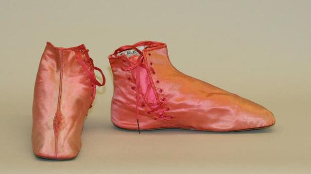 A pair of women's silk boots with side lacing. The boots only come up to the ankle, and end in a squared toe. They appear to be a sort of soft coral pink, but the visible tongue (which would have been hidden when the shoes were worn) is almost a shocking pink.