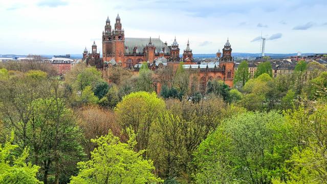 An ornate turretted Victorian building rising above spring trees in a Glasgow park.