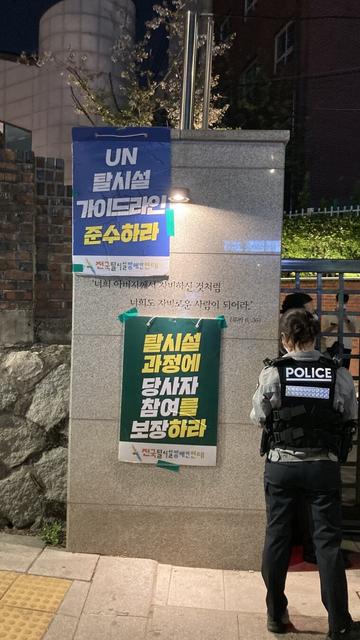 "너희 아버지에게 자비하긴 것처럼 너희도 자비로운 사람이 되어라"라는 성경 구절이 새겨진 혜화동성당 입구 위아래로 전국탈시설장애인연대 피켓 두 개가 붙어있다. "UN 탈시설 가이드라인 준수하라", "탈시설 과정에 당사자 참여를 보장하라"