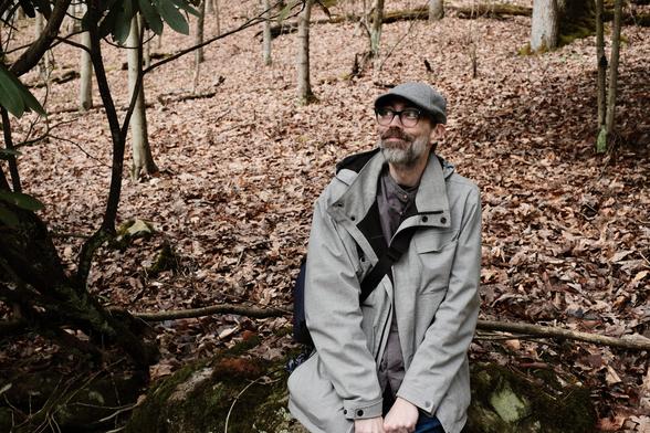 a handsome man wearing a grey felt cap and grey jacket is smiling and looking into the distance at Frank Lloyd Wright's Falling Water in Western Pennsylvania (aka Pennsyltucky)(it's me, photo credit tracey for swiping my cameras and taking pictures of me occasionally <4)