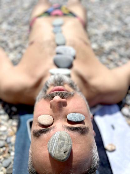 Fotografía tomando el sol con una ristra de piedras encima del cuerpo,  en la frente y en los ojos