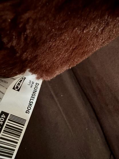 The image features a close-up of a soft, brown, furry bear alongside a visible product tag from IKEA, labeled "Djungelskog." The background appears dark.