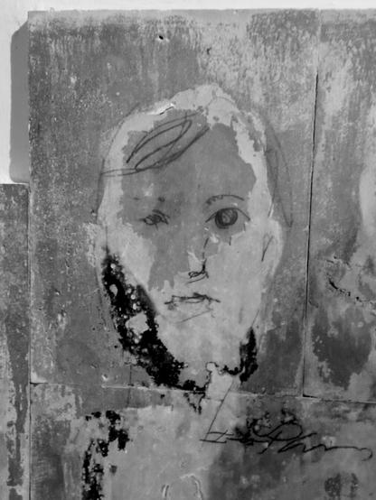 Foto en blanco y negro de un rostro en una pared, que parece que tiene barba, y que está formado por manchas del muro y por trazos de rotulador que le dan forma.