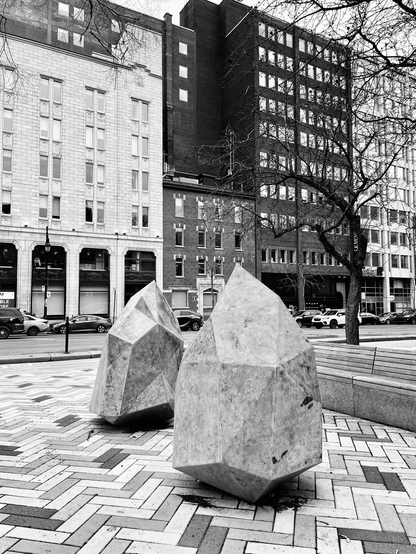 A black and white photography shows 2 sculptures in the shape of rocks on a street of downtown Montreal.