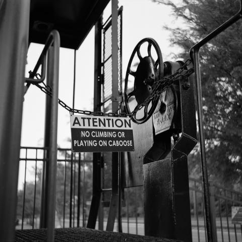 An attention sign warning to not climb on the caboose, with a large metal wheel or valve of some kind