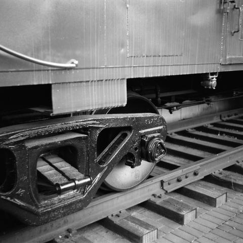 A view of one of the wheels of the caboose, the rail beneath it, and the splotchy, weathered side of the caboose