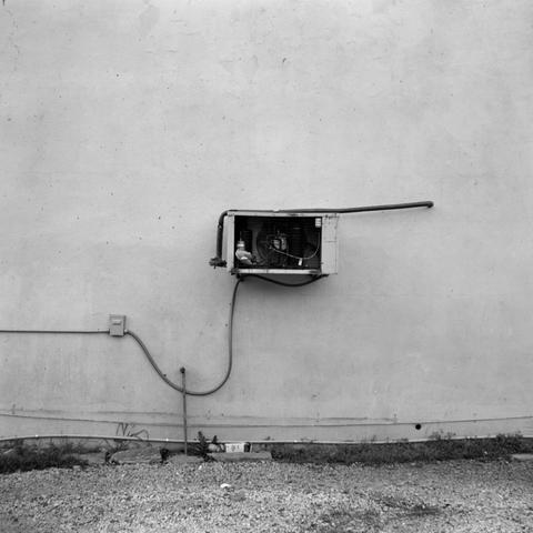A blank wall with a single AC unit stuck onto the side of it.