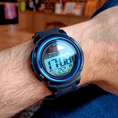 A circular, digital wristwatch in a hairy wrist.