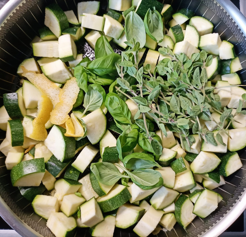 in einer Pfanne Zucchinistücke, Oregano-Zweige, Basilikum und einige Stücke abgeschälte Zitronenschale