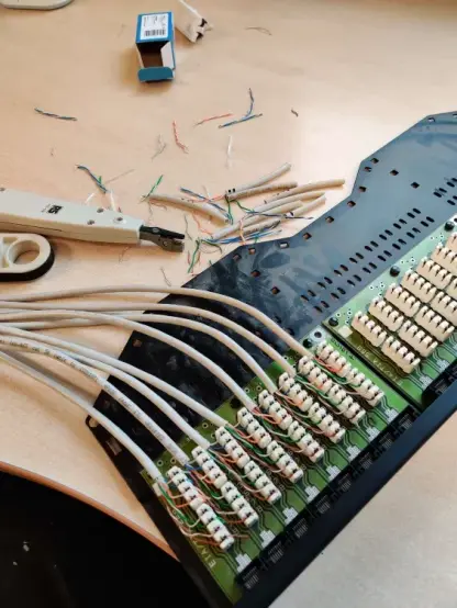 Inside of a network patch panel that is sitting on a desk. The first 8 of 24 slots have cables terminated in the punch-down sockets. Also on the desk are network cabling tools.