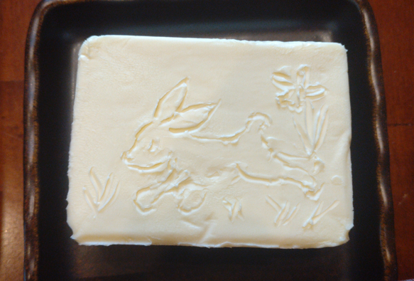 Ein hoppelnder Hase, ein Blümchen und ein bisschen Gras in einen Butterblock geritzt.