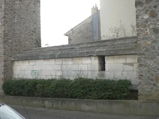 The image shows a stone building or structure with a wall featuring a small window or opening. The structure appears to be made of light-colored stones, and there are some plants or bushes in front of it. In the background, there's a more modern building visible. The overall setting looks urban, possibly in a residential area.

Image Credits: Wikimedia / L’auteur n’a pas pu être identifié automatiquement. Il est supposé qu'il s'agit de : DurandMatthieu (étant donné la revendication de droit d’auteur). / CC BY 2.5
