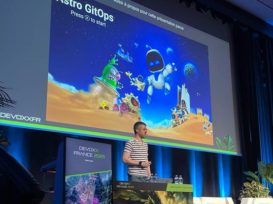 Image de Kevin, sur scène à devoxxfr avec pour fond le slide d'intro, étant la cover officielle du jeu Astrobot sorti sur PS5